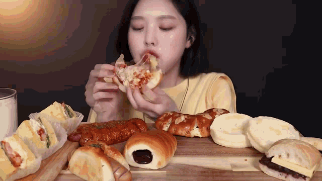 a woman is sitting at a table eating bread and sandwiches