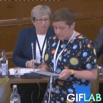 a woman in a space themed shirt is standing in front of a microphone at a conference .