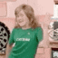 a young girl wearing a green shirt is standing in a kitchen .