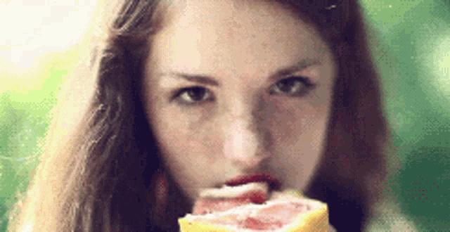 a close up of a woman eating a grapefruit slice