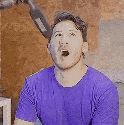 a man in a purple shirt is talking into a microphone with his mouth open .