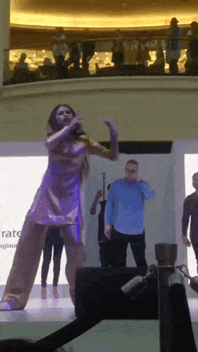 a woman in a gold dress is singing into a microphone while a man in a blue shirt stands behind her