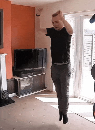 a man in a black shirt is jumping in front of a flat screen tv