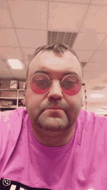 a man wearing pink sunglasses and a purple shirt has a smiley face on his shirt