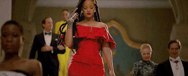 a woman in a red dress is walking down a hallway surrounded by people in tuxedos .