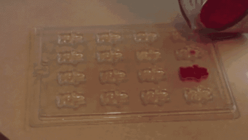 a person pouring red liquid into a pyrex measuring cup filled with gummy bears