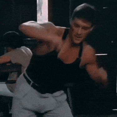 a man in a black tank top is standing in front of a window .