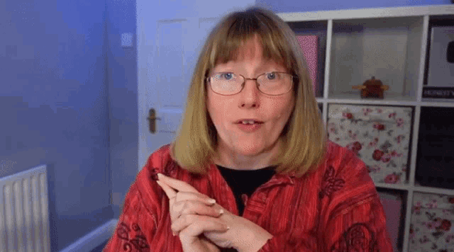 a woman wearing glasses and a red shirt points to the right