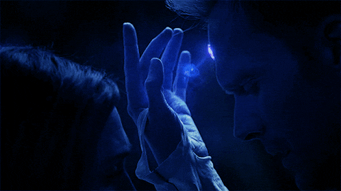 a person holding another person 's hand with a blue light coming out of their eyes