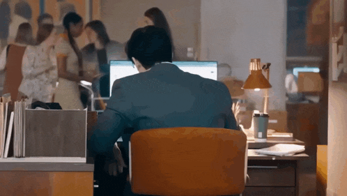 a man in a suit sits at a desk in front of a computer monitor