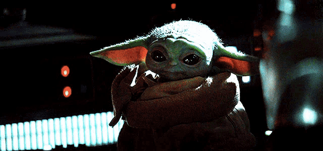a baby yoda is being held in someone 's hand in a dark room