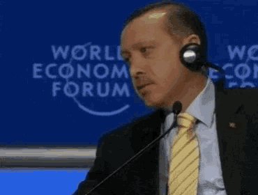 a man speaking into a microphone in front of a world economic forum sign