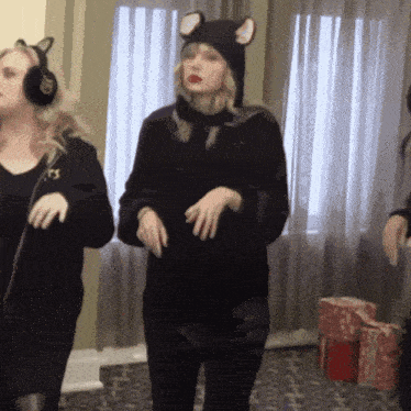 a woman wearing a cat hat and ear muffs is dancing in front of a window
