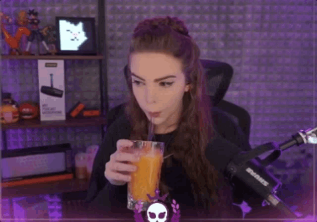 a woman drinking orange juice through a straw in front of a microphone