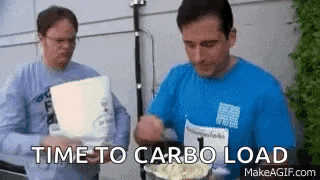 two men are standing next to each other eating popcorn and one of them is holding a bowl of popcorn .