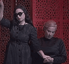 two women are standing next to each other holding hands in front of a red wall .