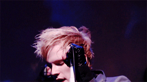 a close up of a person singing into a microphone with their eyes closed
