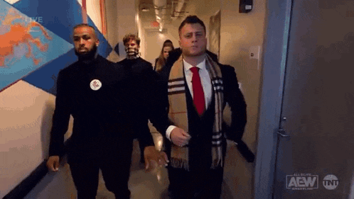 a group of men in suits and scarves are walking down a hallway together .