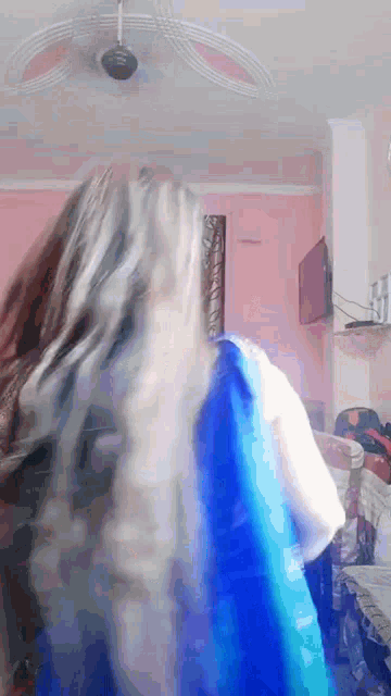 a woman in a blue dress is standing in a room with a ceiling fan