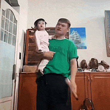 a man in a green shirt is holding a baby on his shoulders .
