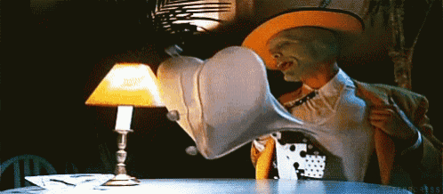 a man with a mask on his face is sitting at a table holding a pillow in front of a lamp .