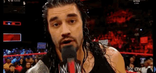 roman reigns is talking into a microphone while standing in a wrestling ring .