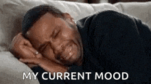 a man is crying while laying on a couch with the words `` my current mood '' written above him .