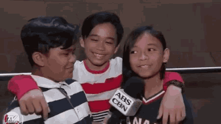 three young boys and a girl are posing for a picture while talking into a microphone .