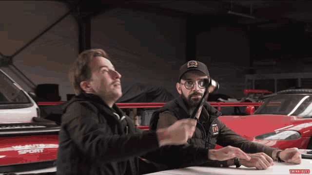 two men are sitting in front of a sports car