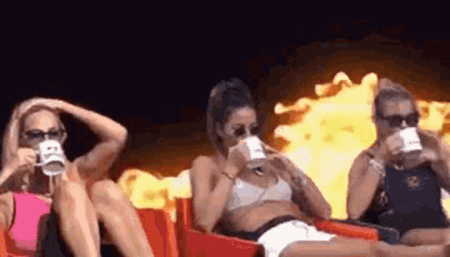 three women are sitting in red chairs drinking coffee while watching a movie .