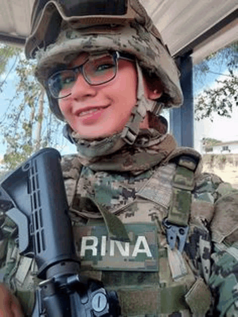 a woman in a military uniform and helmet is holding a gun and smiling .