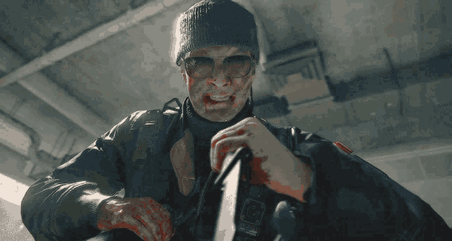a man wearing sunglasses and a beanie is holding a gun
