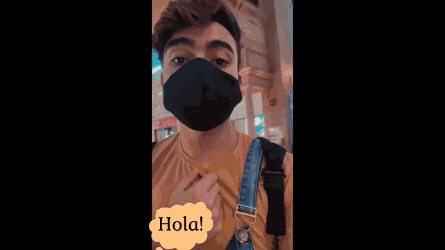a man wearing a black face mask with a yellow speech bubble that says hola