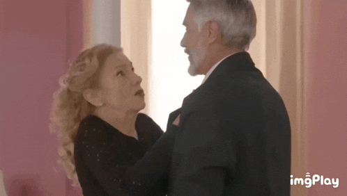 a man in a suit and a woman in a black dress are dancing in front of a window .