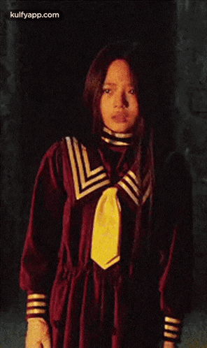 a girl in a red dress with a yellow tie is standing in a dark room ..