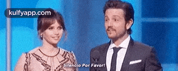 a man and a woman are standing next to each other on a stage and the man is saying silence por favor .