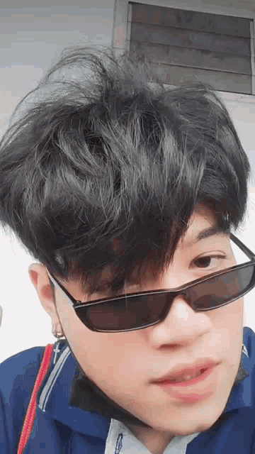 a young man wearing sunglasses and a blue shirt is looking at the camera