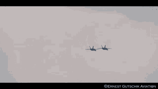 two fighter jets flying in a cloudy sky with ernest gutschik aviation written on the bottom right