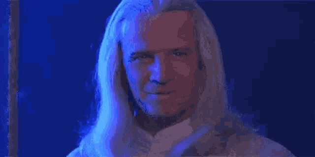 a man with white hair is standing in front of a blue light .