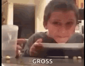 a young boy is sitting at a table with a bowl of food and looking at the camera .