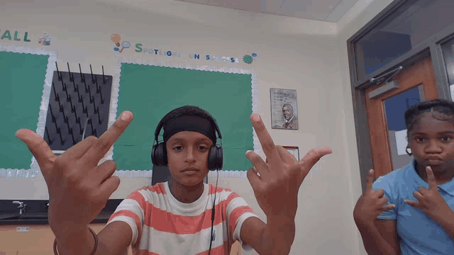 a boy wearing headphones stands in front of a bulletin board that says " all " on it