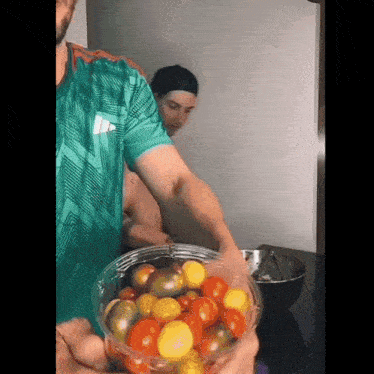 a man in a green shirt is holding a plastic bowl of tomatoes