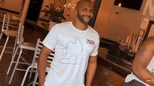 a man wearing a white arby 's t-shirt stands in a restaurant