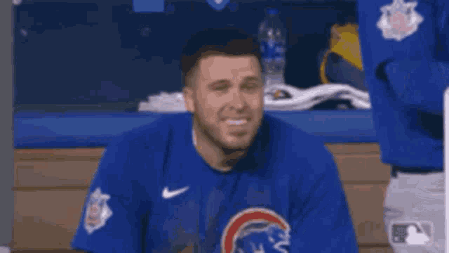 a man wearing a blue cubs shirt is sitting in the dugout