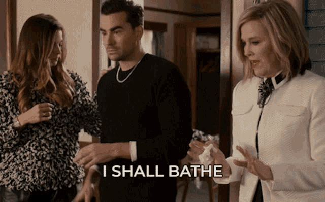 a man in a black sweater stands next to a woman in a white jacket and says i shall bathe
