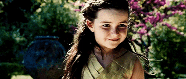 a young girl in a yellow dress is smiling in front of purple flowers