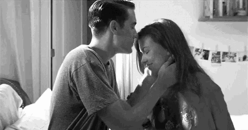 a black and white photo of a man kissing a woman on the forehead on a bed .
