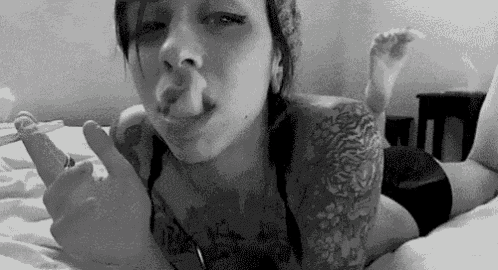 a black and white photo of a woman smoking a cigarette while laying on a bed .