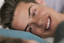 a close up of a young man laying on a bed with his mouth open