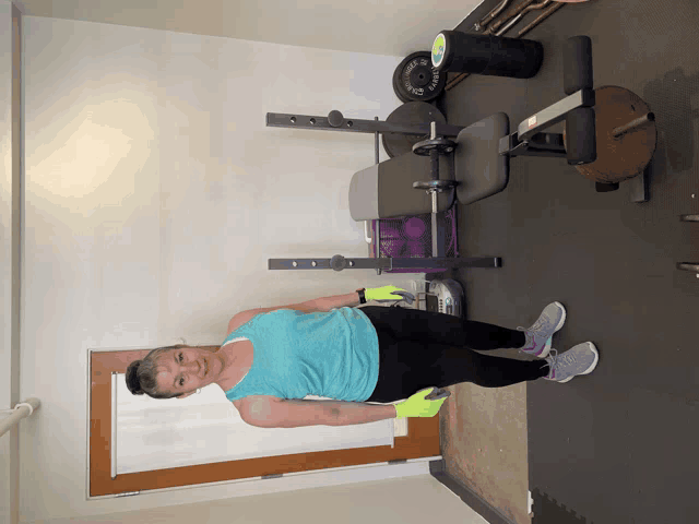 a woman in a blue tank top is standing in front of a bench with a barbell that says ' rogue '